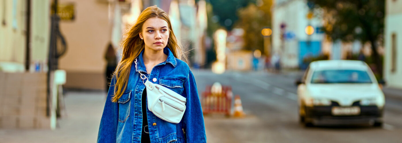 girl in a denim jacket and waist bag walks through the city along the road
