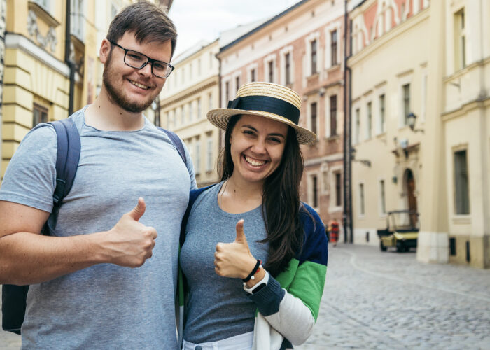 cheerful couple stand with thumb up at old european street