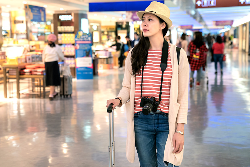 woman wearing a red striped shirt and hat stands at the airport.