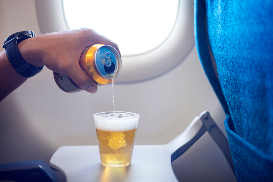 man pouring beer from can into a glass on airplane.