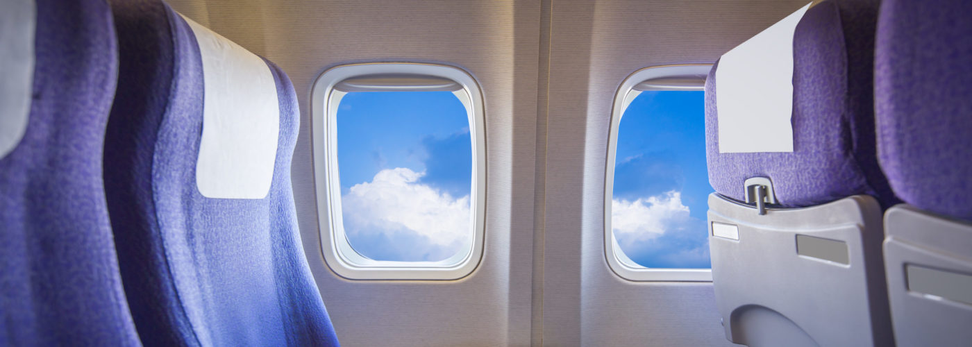 Empty row of plane seats with blue sky as seen out the window