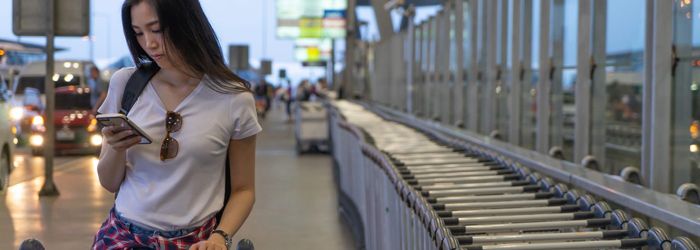 woman on phone at airport with luggage trolley