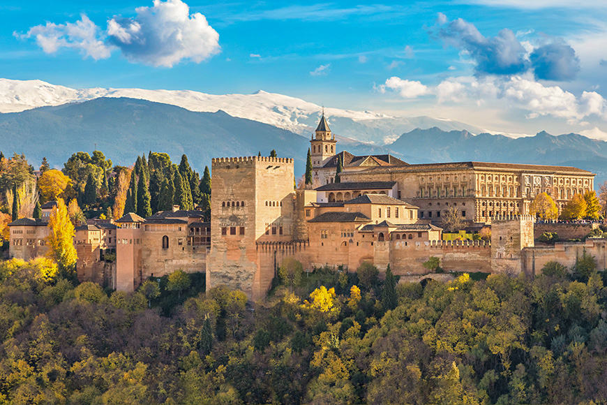 Alhambra - medieval Moorish fortress surrounded by yellow autumn trees with snow mountains on background, Granada, Andalusia, Spain 