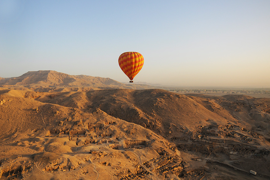 Orange hot air balloon riding over the desert and ruins in Luxor Egypt