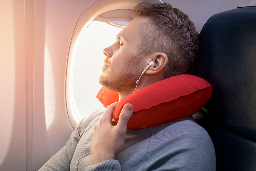 Male passenger of airplane listens to music and enjoys pillow for sleeping in chair