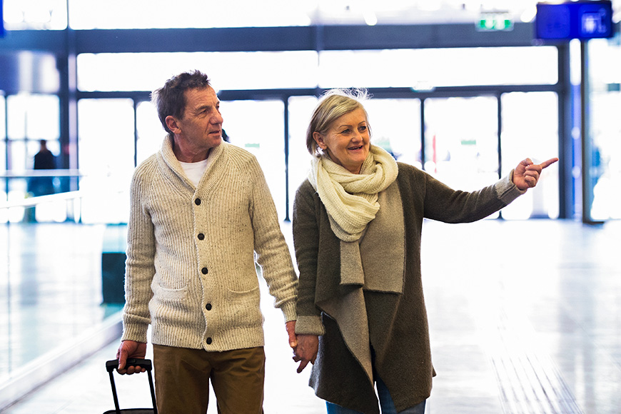 senior couple walking through airport pointing wearing scarf and sweaters