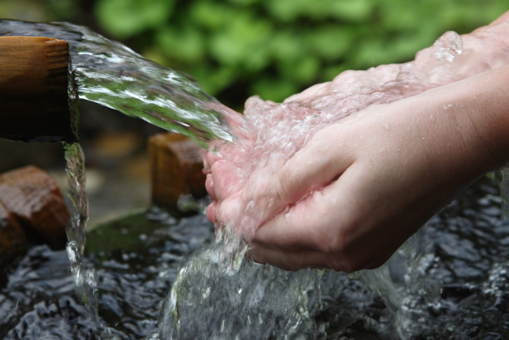 Person rinsing their hands in fresh water from an outdoor pipe
