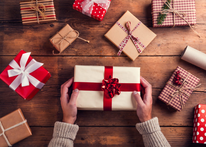 Aerial view of hands holding a gift surrounded by other affordable holiday travel gifts on a wooden table
