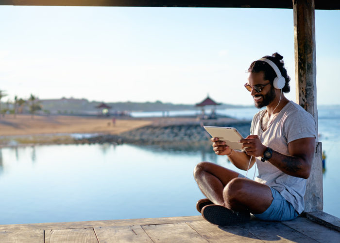 Man watching a video on tablet with headphones on a deck over the ocean