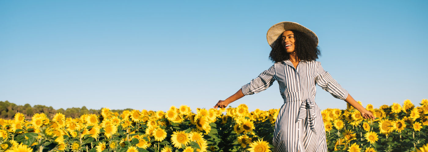 Woman in sundress and sunhat walking through a field of sunflowers on a clear day