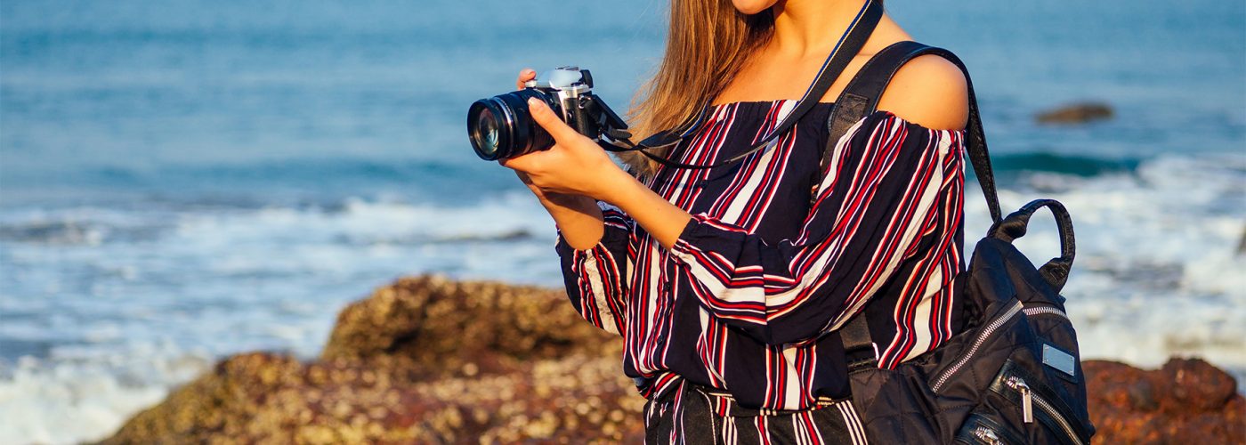 woman in jumpsuit with camera at beach.