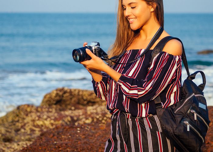 woman in jumpsuit with camera at beach.