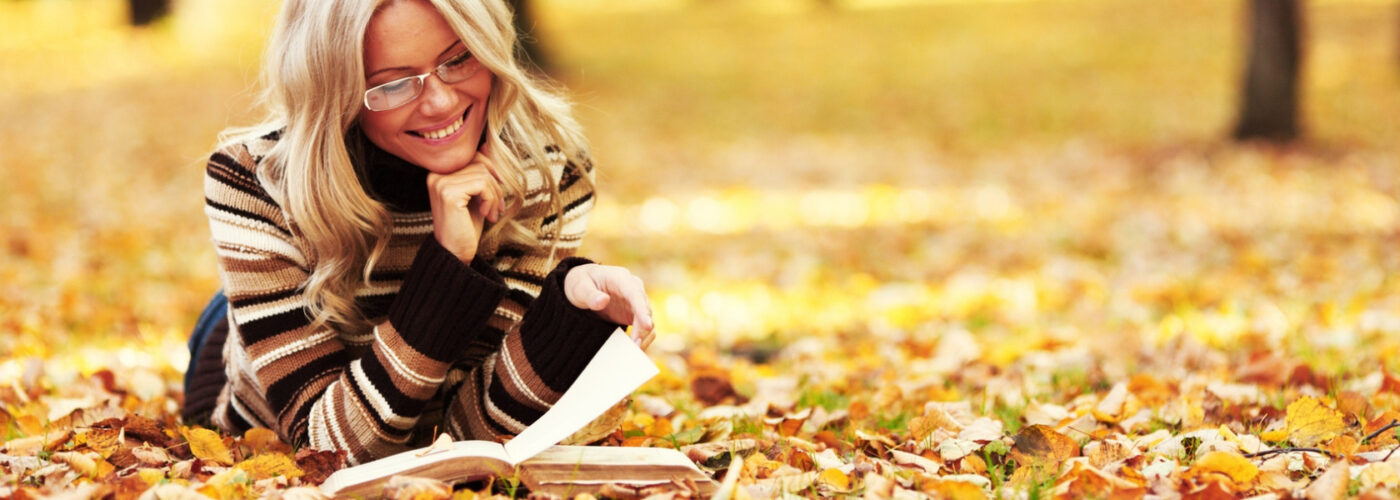 blonde woman reading a book in fall.