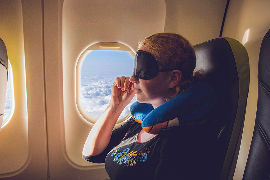 woman using travel pillow and sleeping mask in plane.