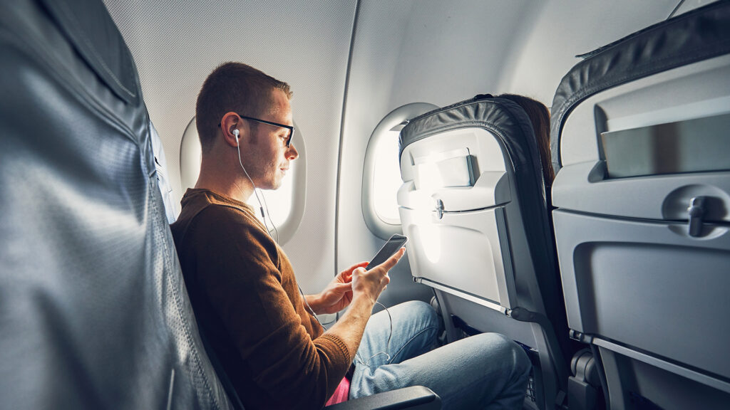man sitting on airplane headphones and phone