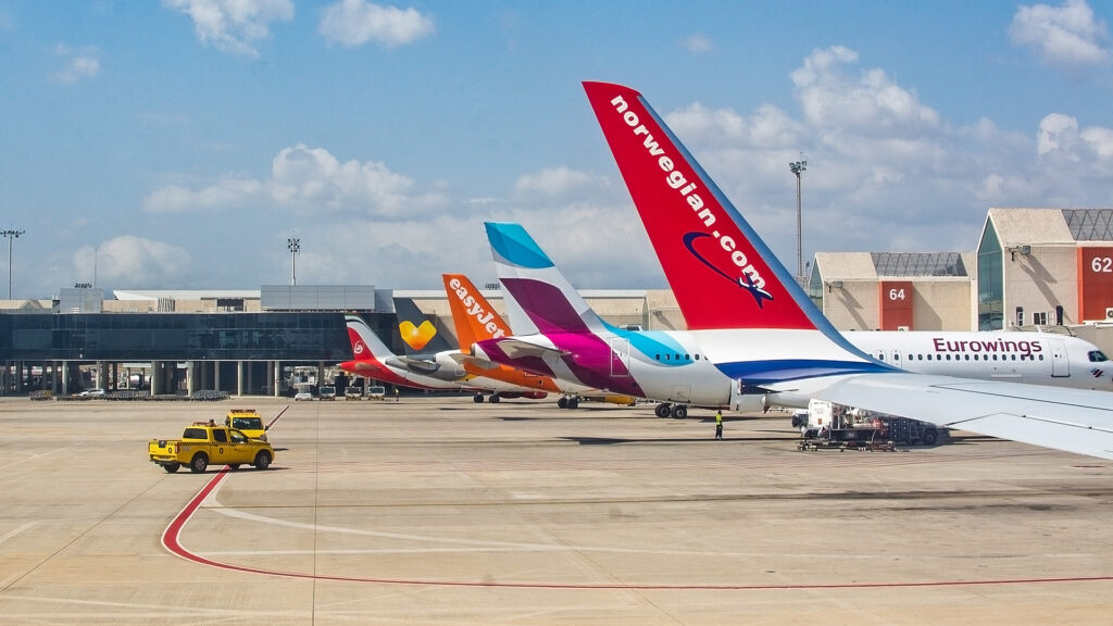 planes parked at airport in a row. Airplane tail fins from Norwegian, Eurowings, Easyjet on the tarmac