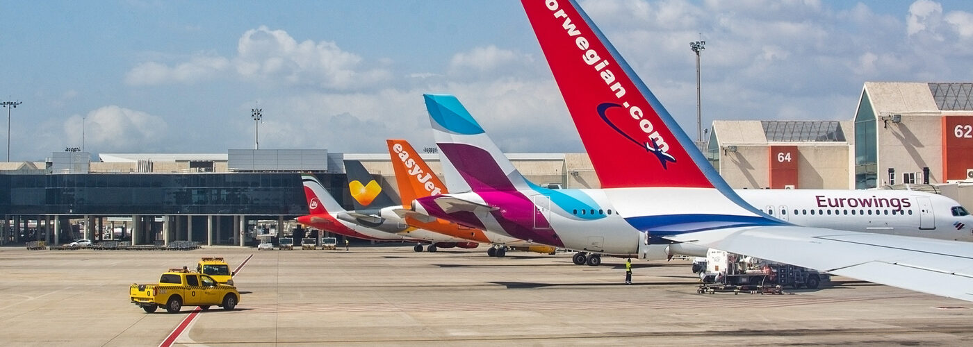 planes parked at airport in a row. Airplane tail fins from Norwegian, Eurowings, Easyjet on the tarmac