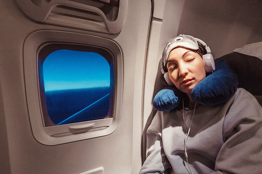 Asian girl sleeping in her seat on the plane near the window in a mask and with a pillow to sleep
