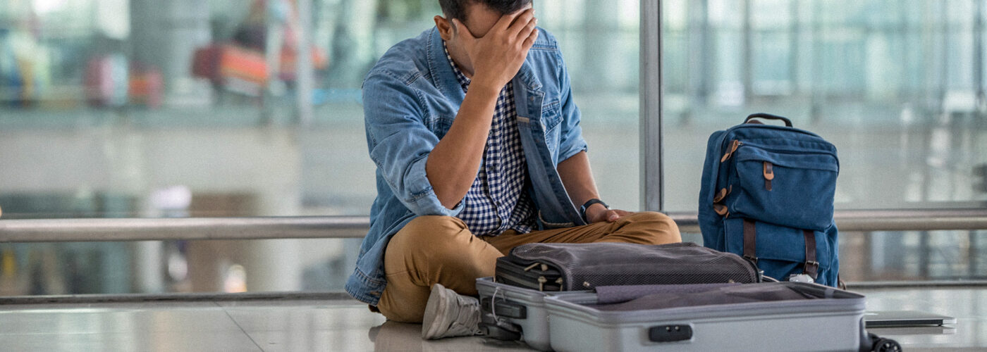 man sitting on floor at airport with open luggage lost item