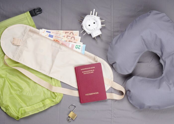 flat lay of travel related items including money belt neck pillow charger passport lock