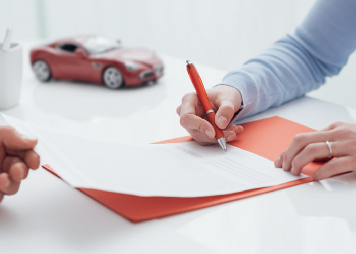 Person signing car rental agreement with a small model car in the background