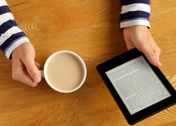 Kindle book on table with cup of coffee.