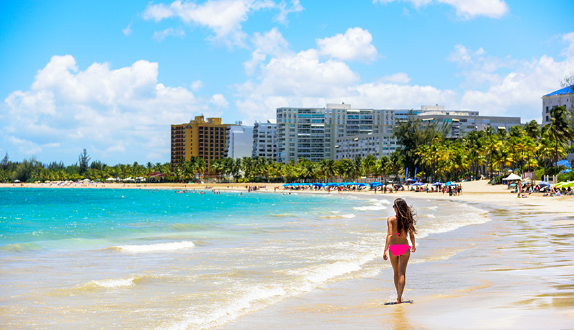 People on Isla Verde resort beach in Puerto Rico. Unrecognizable woman walking down the beach on summer holiday in bikini on famous Hispanic travel destination.
