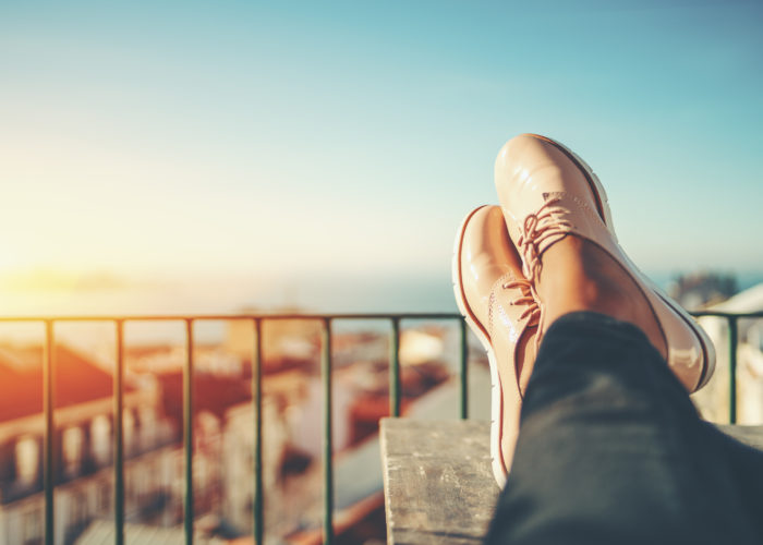 Point of view shot of a person resting their feet on the railing of a balcony overlooking an European city sunset