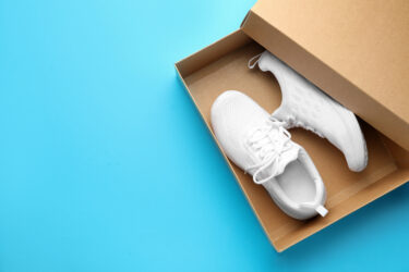 New white shoes inside brown shoe box on a bright blue background