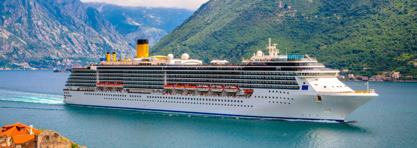Cruise ship in water in front of lush green mountains
