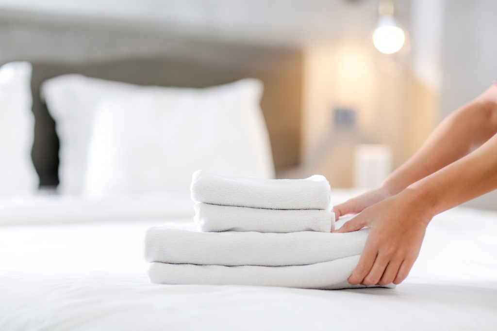 Person placing folded white sheets on white bed