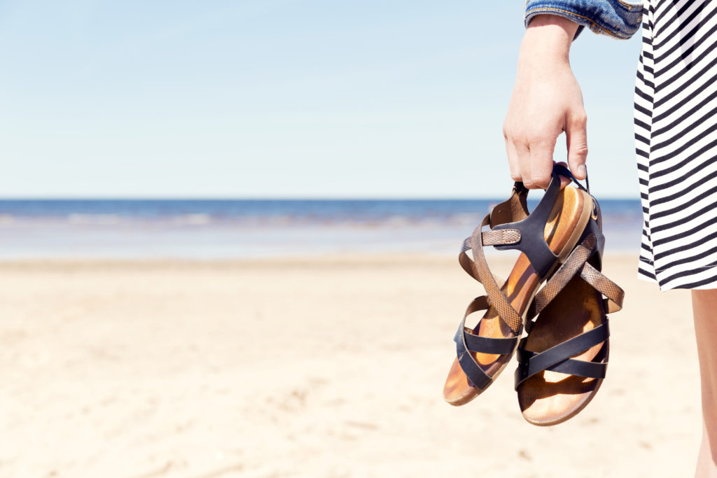 Close up of woman's hands carrying a pair of sandals on the beach