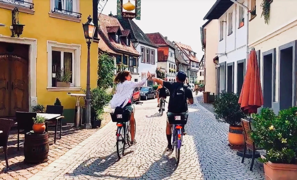 Two people high-fiving on bikes on a cobblestone street