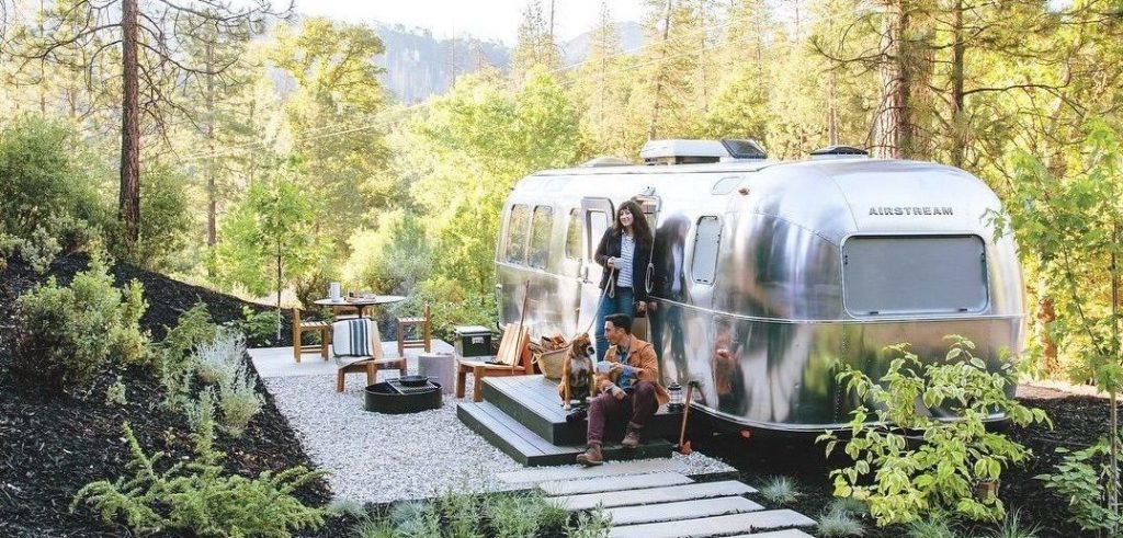 Two people and a dog sitting on the small deck outside an airstream at AutoCamp Yosemite