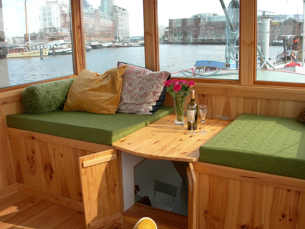 A wooden sitting area arranged with a bottle of wine and two glasses, overlooking a marina in Amsterdam, Netherlands