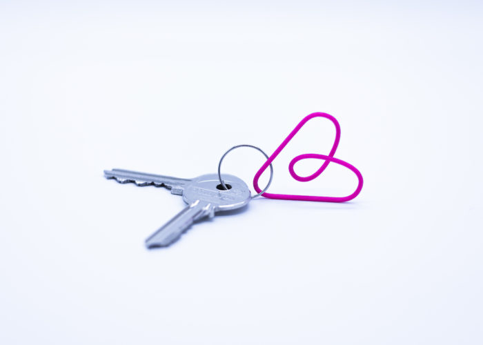 Two house keys attached with a pink paper clip on a white background
