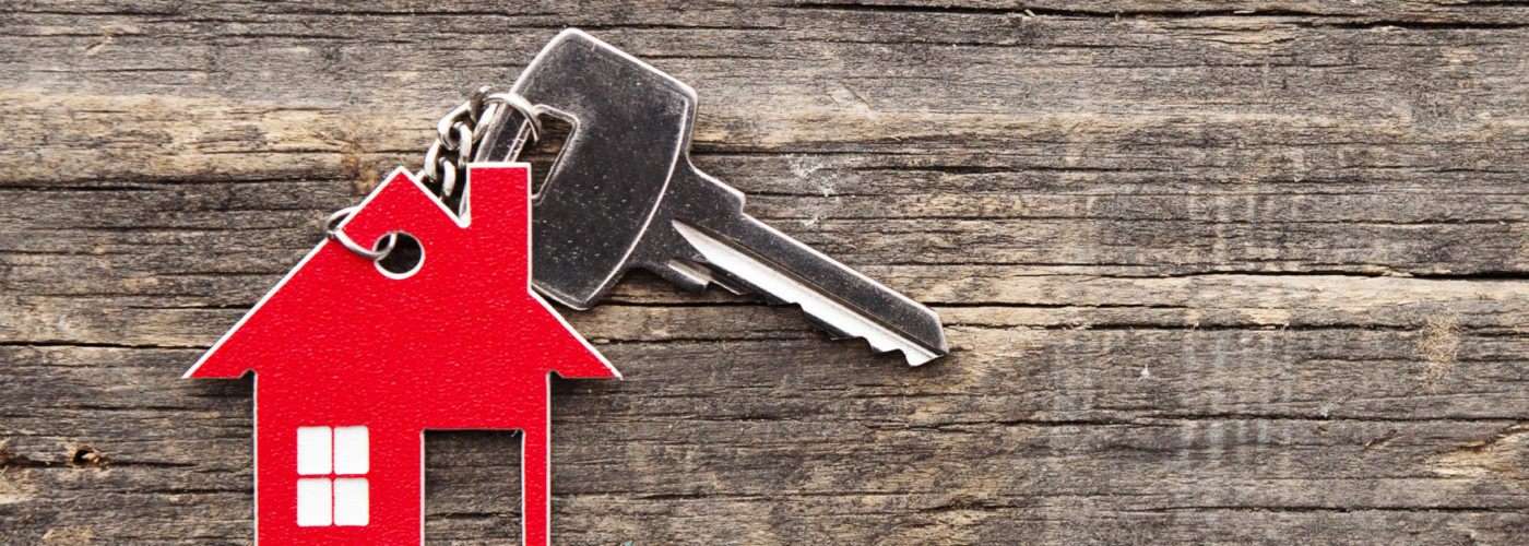 House key with red house-shaped keychain on a wooden background