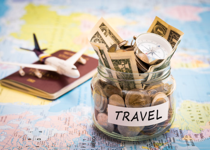 A jar of money labeled "Travel", a passport, and an airplane figurine on a colorful world map