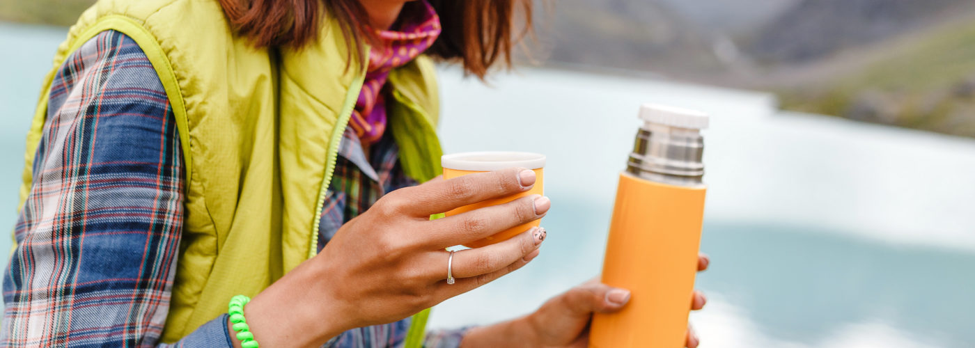 Woman sitting outside drinking from an orange travel thermos