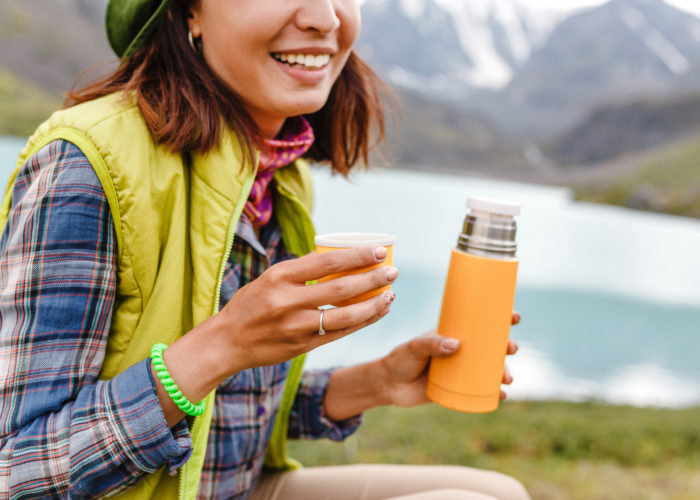 Woman sitting outside drinking from an orange travel thermos