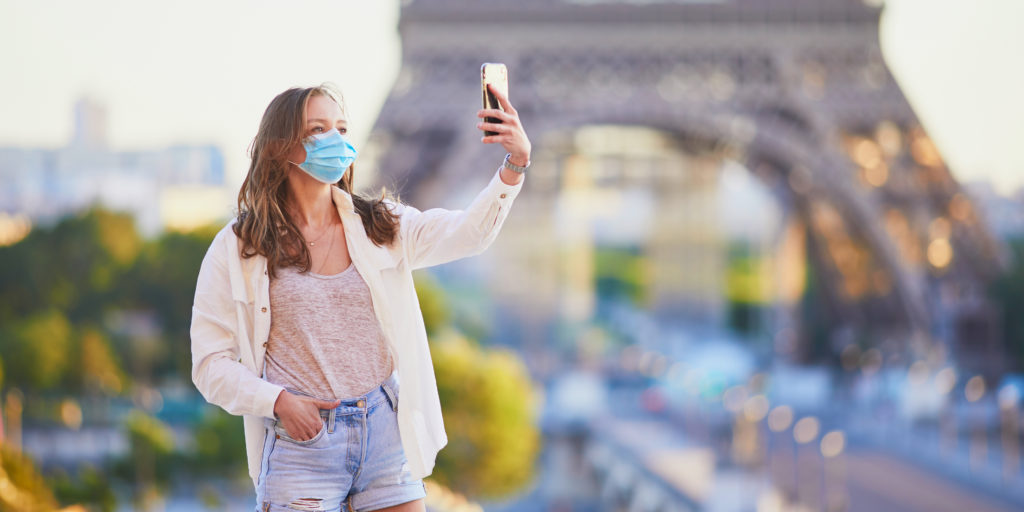 Woman taking a selfie wearing a facemask in front of the Eiffel Tower