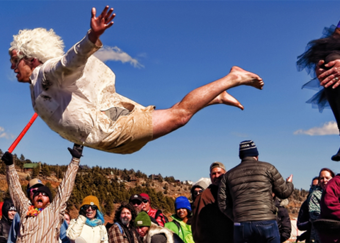 Man jumping from a platform while a crowd cheers on at Frozen Dead Guy Days festival