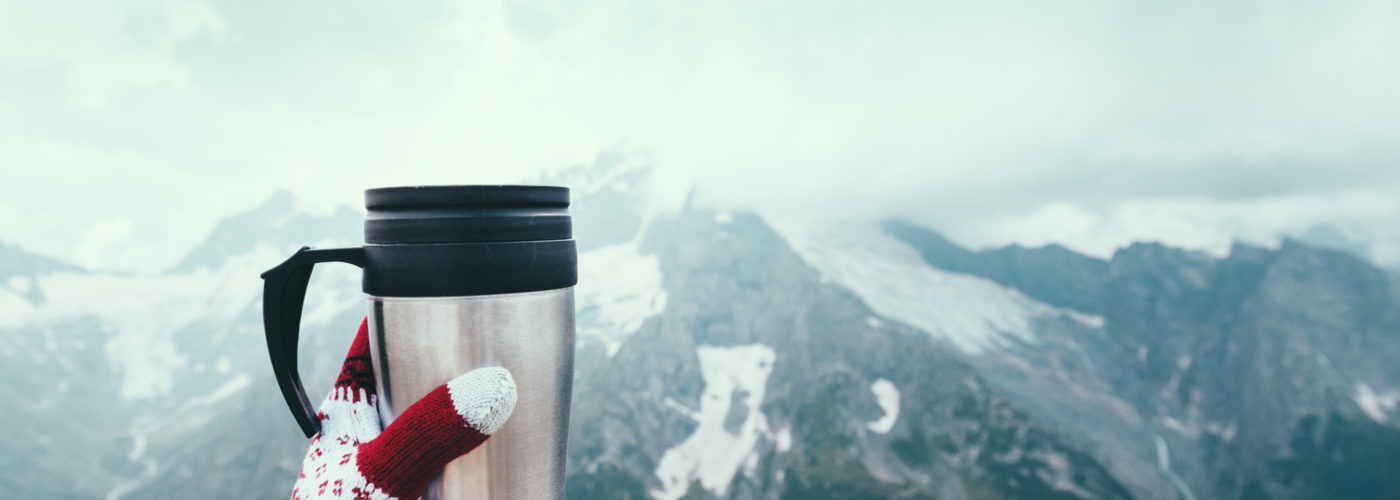 Point of view shot of a person holding a thermos of tea against a mountain backdrop