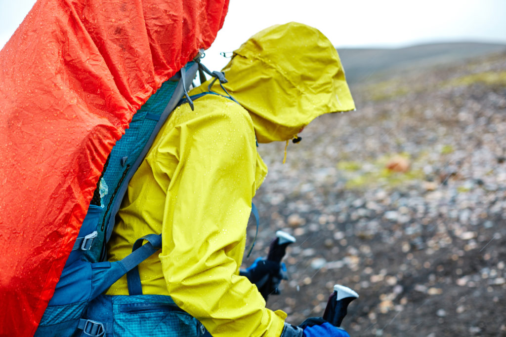 Person hiking in the mountains wearing a waterproof rain coat and a large, tarp-covered backpack