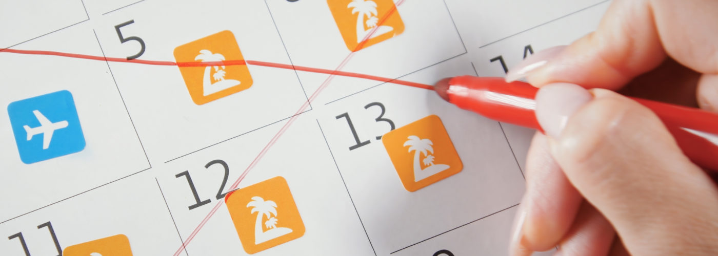 Person crossing out vacation plans on whiteboard calendar