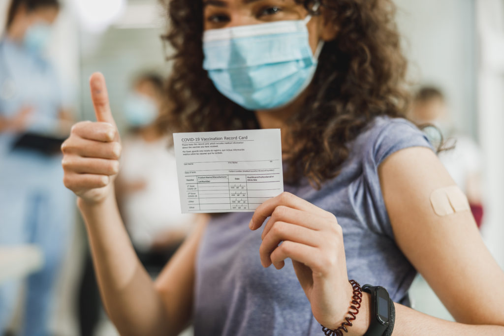 Woman holding up her COVID-19 vaccination card with a thumbs up after receiving her vaccine