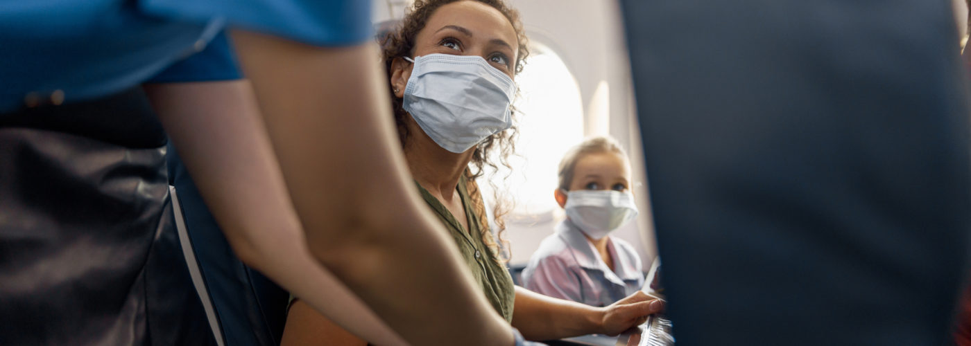Woman and child wearing masks on plane speaking to a flight attendant