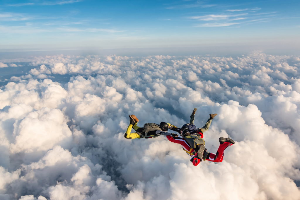 Three people skydiving above the clouds