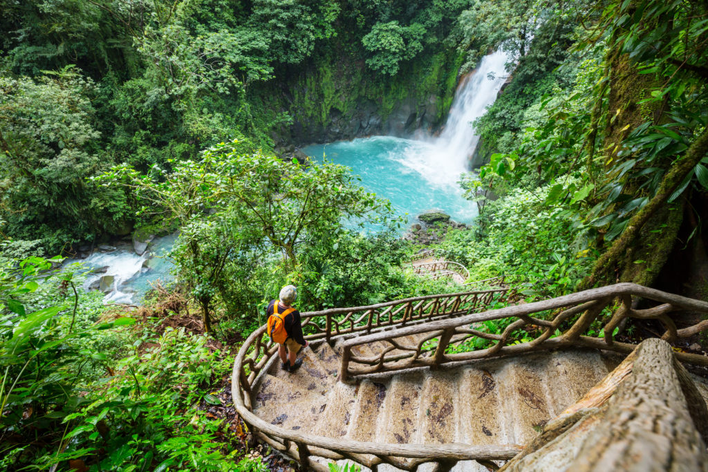 Woman walking down a flight of stairs toward a waterfall in Costa Rica