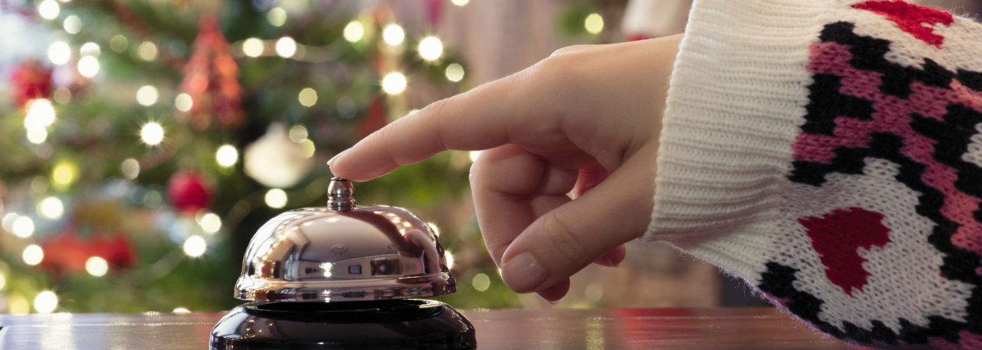 Hand ringing concierge bell at hotel desk with Christmas tree in background